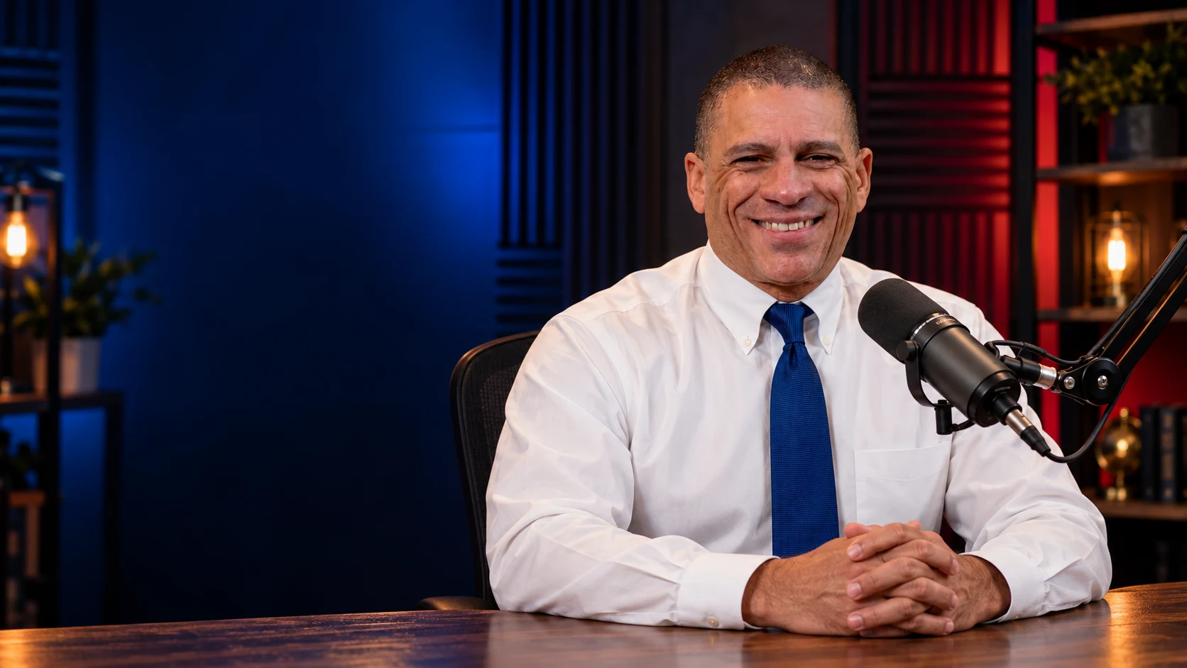 Promotional portrait of Mark seated in a blue and red podcast studio
